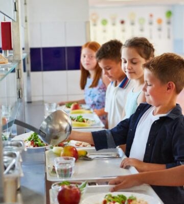 Nearly half of UK parents want more plant-based meals in schools. Photo shows a queue of school children loading their trays with fruit and vegetables