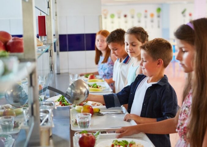Nearly half of UK parents want more plant-based meals in schools. Photo shows a queue of school children loading their trays with fruit and vegetables