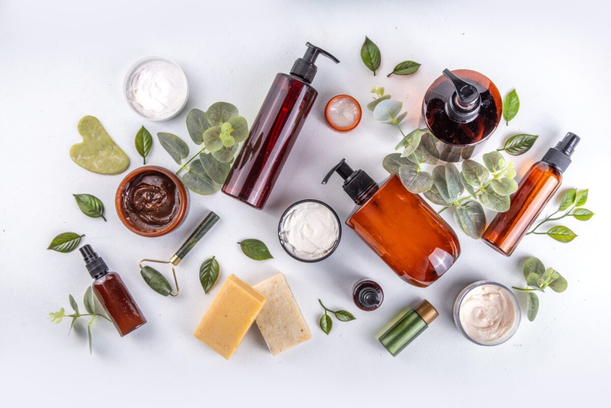 Photo shows a selection of sustainable, label-free beauty products on a white background alongside green leaves