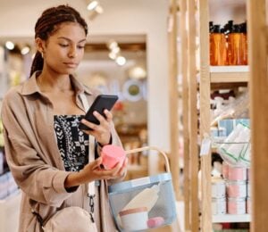 Photo shows a young woman looking up the ingredients of a beauty product on her phone in a store