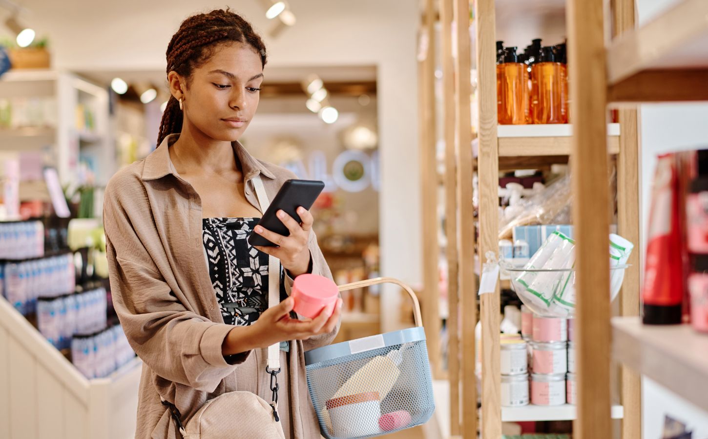 Photo shows a young woman looking up the ingredients of a beauty product on her phone in a store