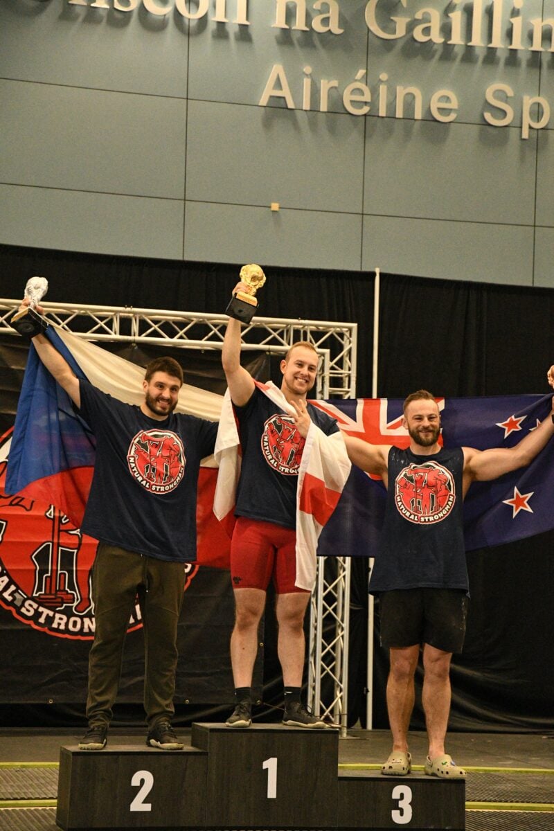 Photo shows plant-based athlete Tom Butts, who just became the vegan World’s Strongest Man, on the podium alongside his competitors