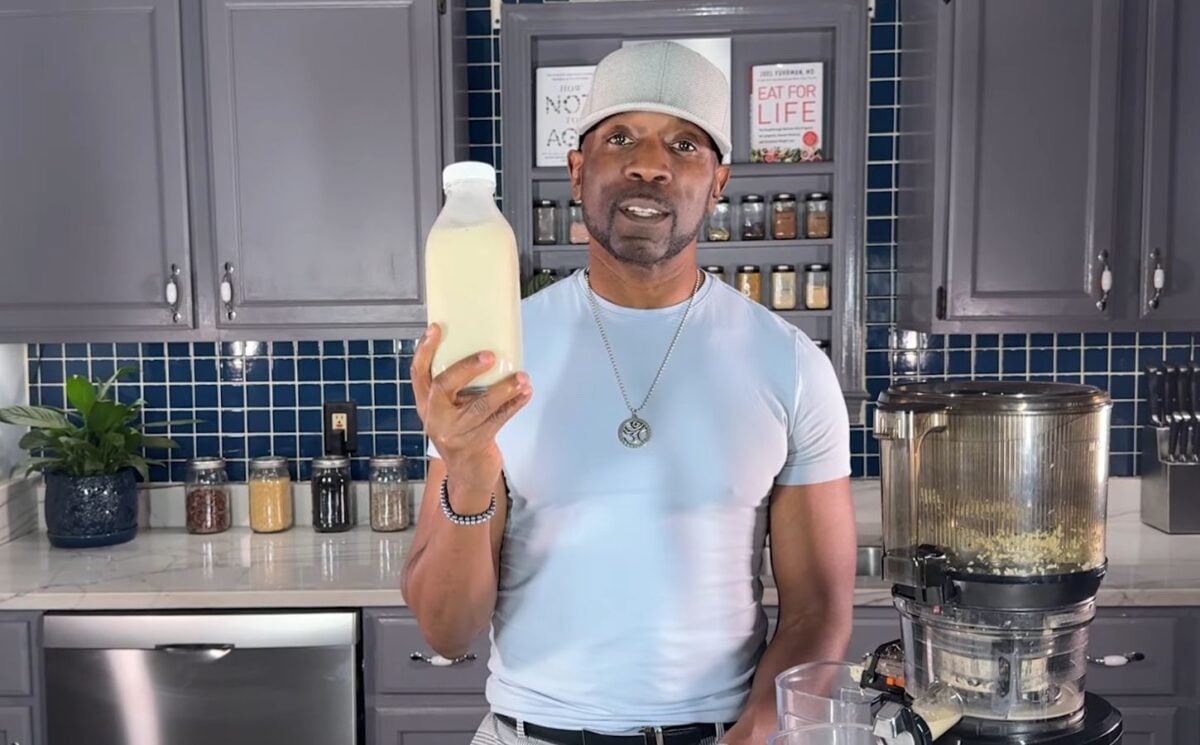 Javant holds a bottle of homemade vanilla hemp milk in his kitchen beside a juicer