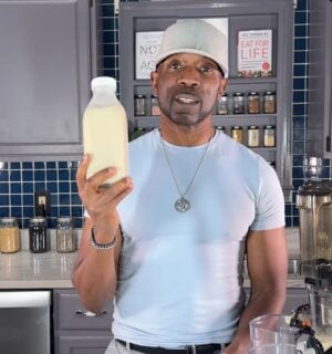 Javant holds a bottle of homemade vanilla hemp milk in his kitchen beside a juicer