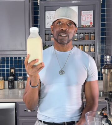 Javant holds a bottle of homemade vanilla hemp milk in his kitchen beside a juicer
