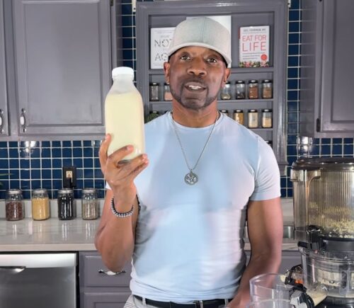 Javant holds a bottle of homemade vanilla hemp milk in his kitchen beside a juicer