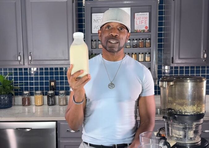 Javant holds a bottle of homemade vanilla hemp milk in his kitchen beside a juicer