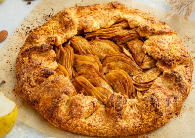 an image of an almond pear galette with slices of almond and pear surrounding the tart for cozy vegan bakes for afternoon tea