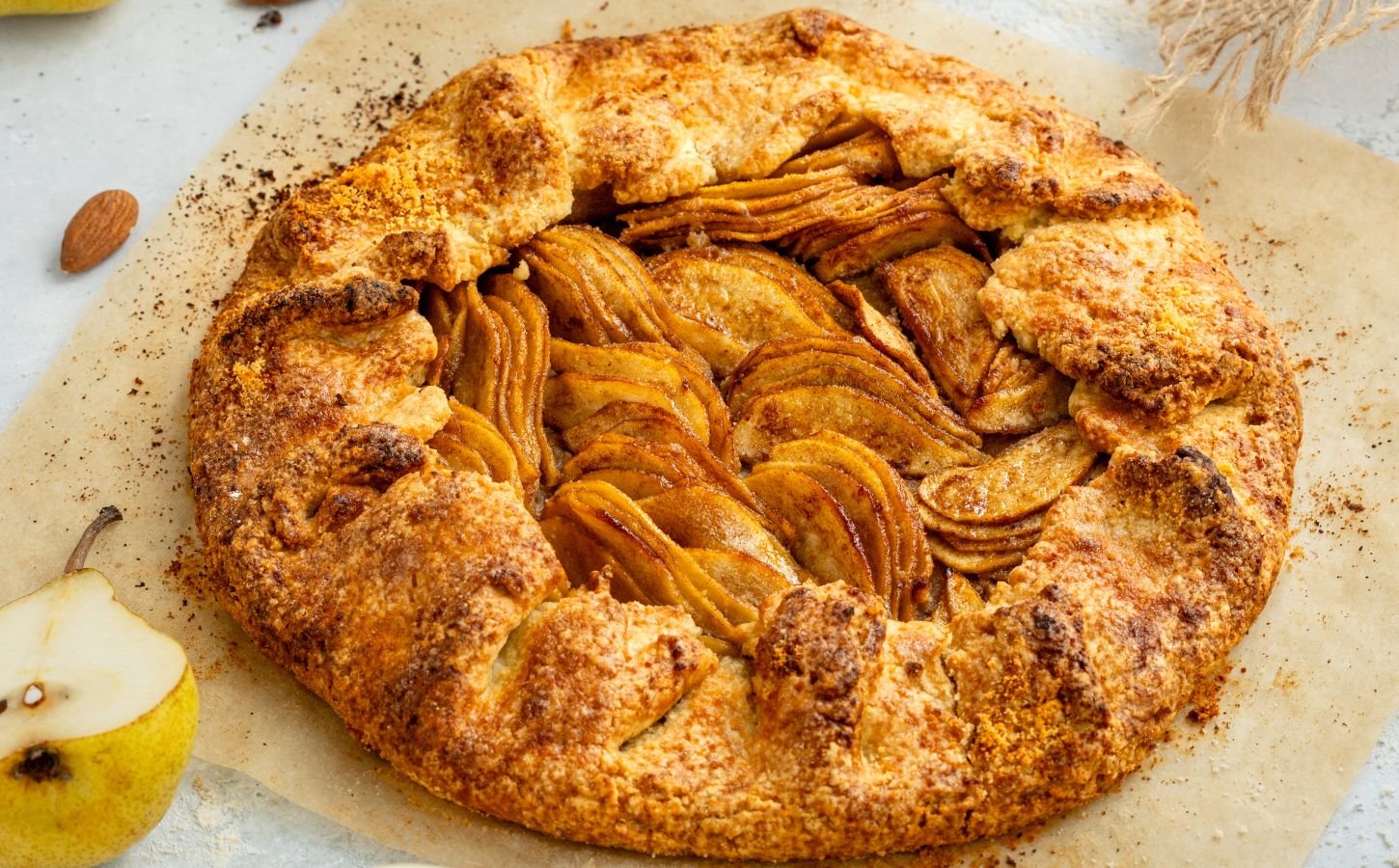 an image of an almond pear galette with slices of almond and pear surrounding the tart for cozy vegan bakes for afternoon tea