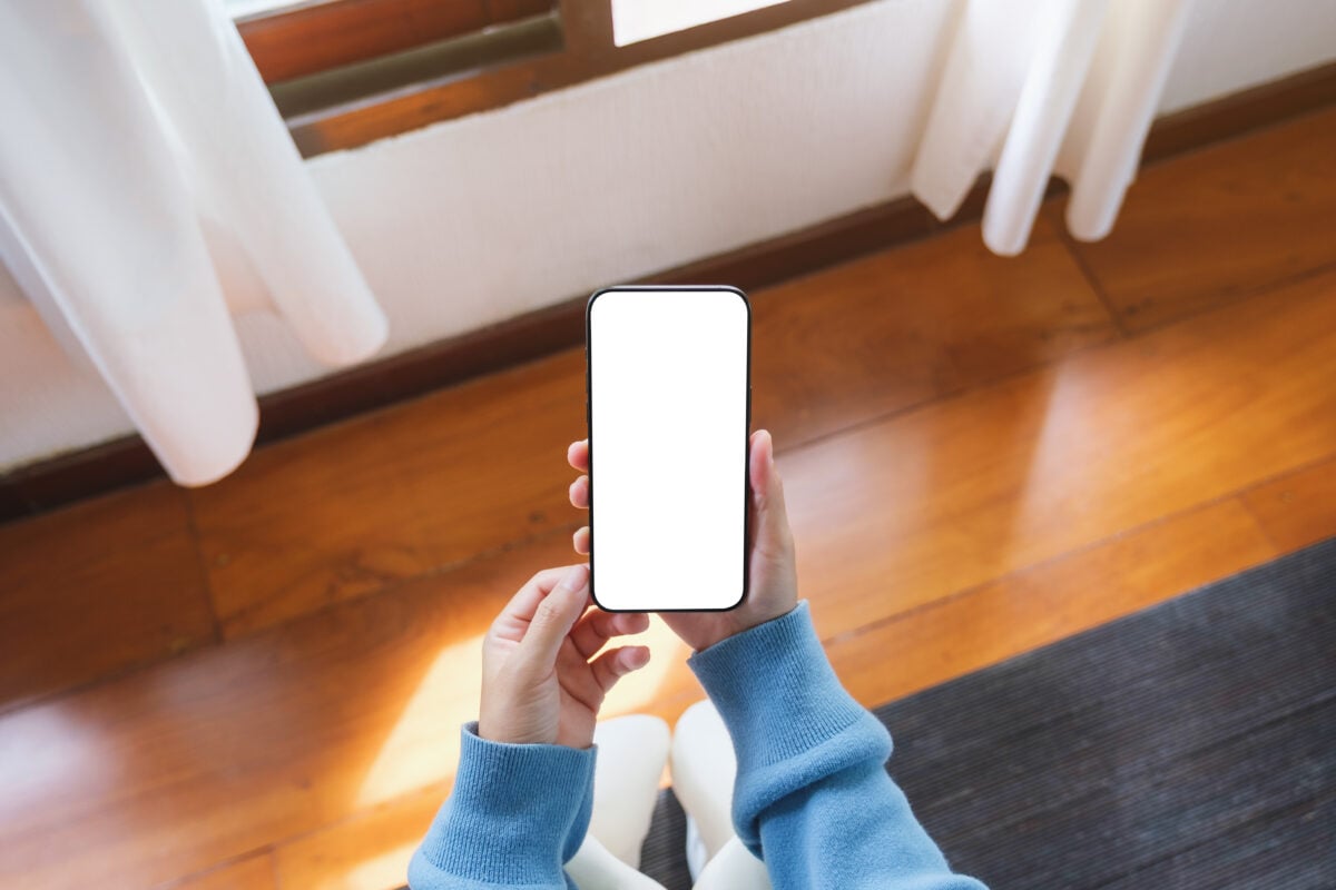 Photo shows a woman's hands as she holds a smart phone with a blank white screen