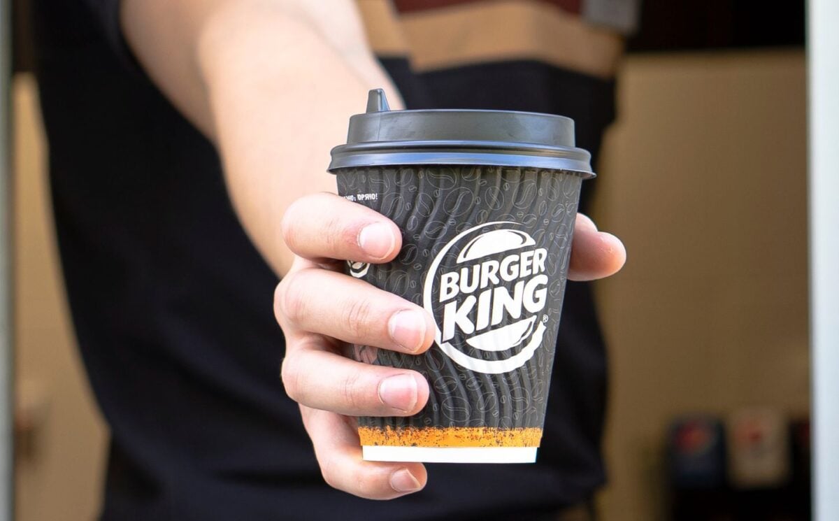 Photo shows a Burger King employee passing coffee in a branded BK paper cup out of the drive-thru window. Burger King Austria has gone back on its pledge to replace dairy with oat milk after one week.