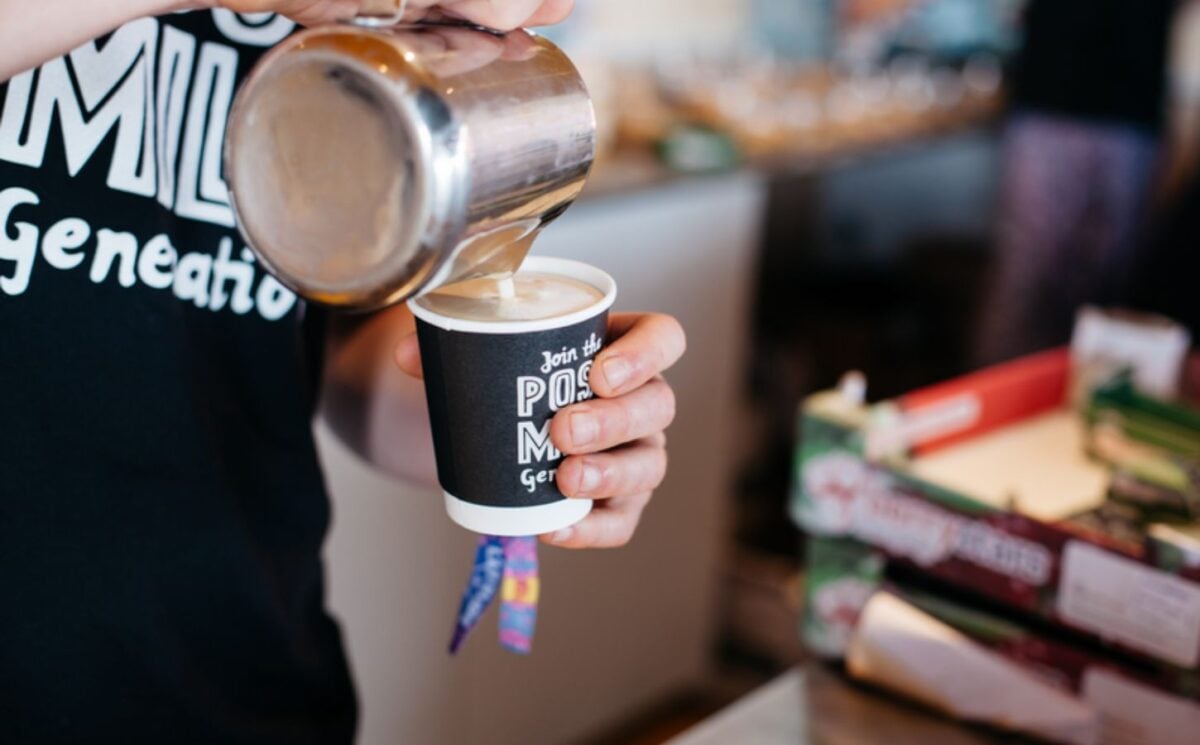 Photo shows a barista making a cup of coffee with foamed Oatly oat milk
