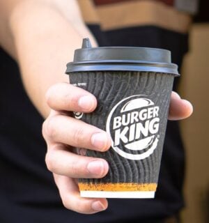 Photo shows a Burger King employee passing coffee in a branded BK paper cup out of the drive-thru window. Burger King Austria has gone back on its pledge to replace dairy with oat milk after one week.