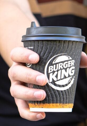 Photo shows a Burger King employee passing coffee in a branded BK paper cup out of the drive-thru window. Burger King Austria has gone back on its pledge to replace dairy with oat milk after one week.