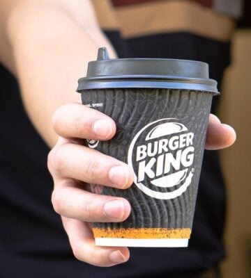 Photo shows a Burger King employee passing coffee in a branded BK paper cup out of the drive-thru window. Burger King Austria has gone back on its pledge to replace dairy with oat milk after one week.