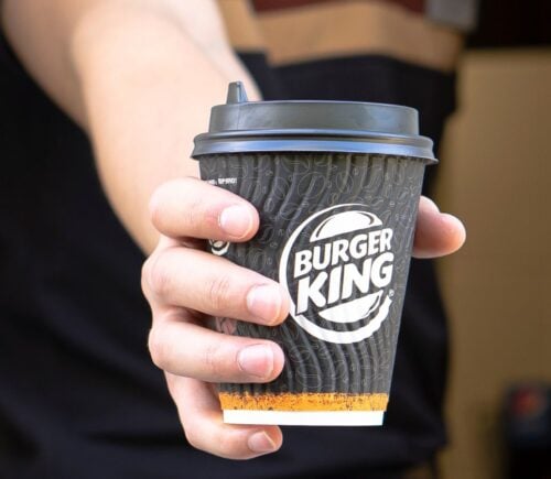 Photo shows a Burger King employee passing coffee in a branded BK paper cup out of the drive-thru window. Burger King Austria has gone back on its pledge to replace dairy with oat milk after one week.