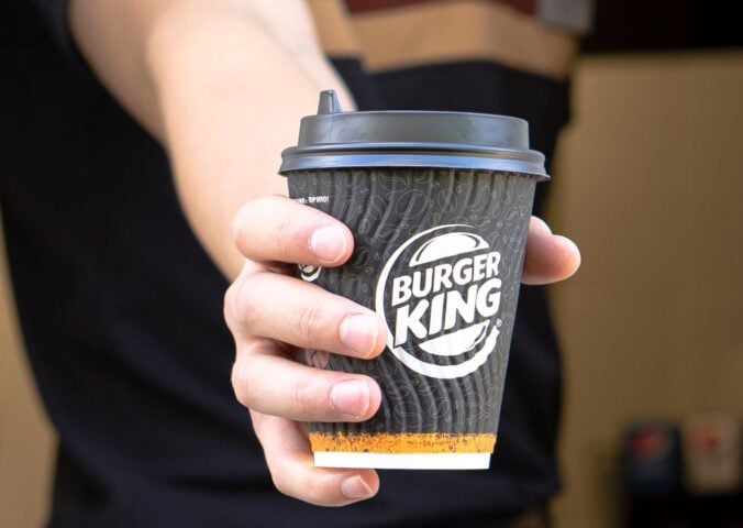 Photo shows a Burger King employee passing coffee in a branded BK paper cup out of the drive-thru window. Burger King Austria has gone back on its pledge to replace dairy with oat milk after one week.