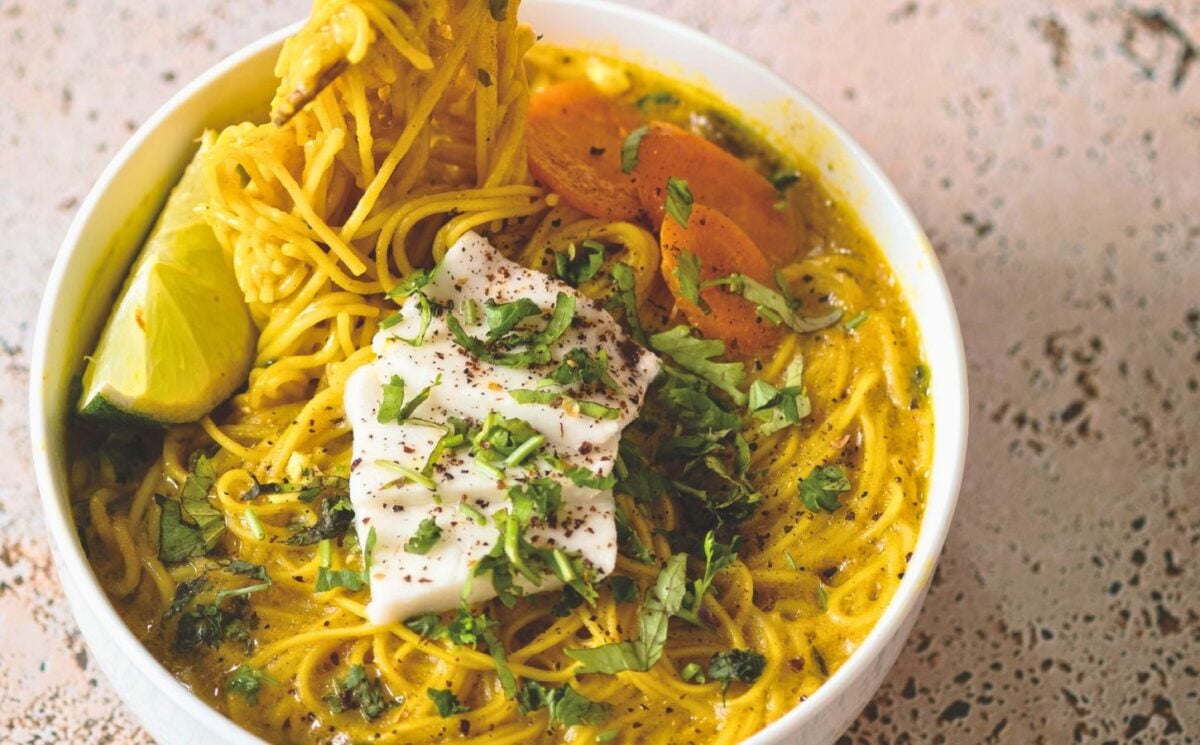 a bowl of vegan creamy coconut curry ramen with carrot, soft tofu, lime, and herbs for cozy lunch recipes for fall