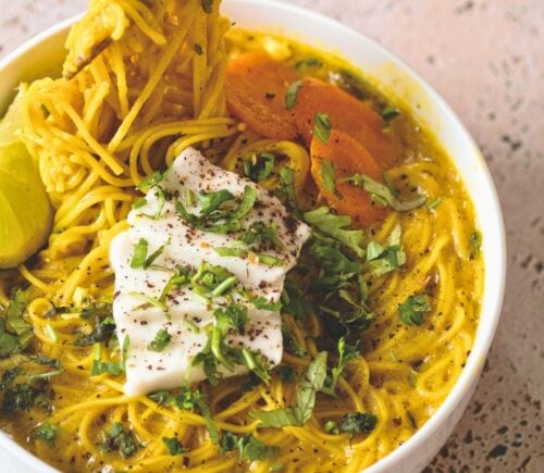 a bowl of vegan creamy coconut curry ramen with carrot, soft tofu, lime, and herbs for cozy lunch recipes for fall