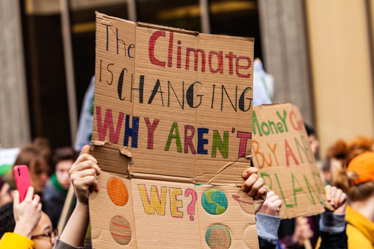 Photo shows a cardboard sign that reads "the climate is changing why aren't we?"