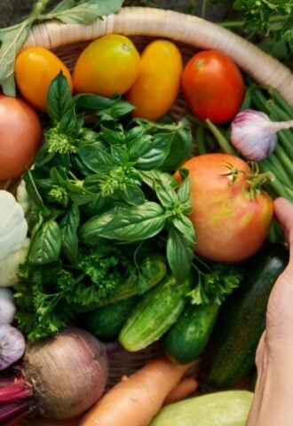 Photo shows someone's hands in a basket of freshly picked herbs and vegetables