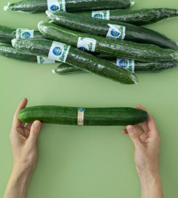 Photo shows someone's hands holding a cucumber wrapped in Saveggy's edible, plastic-free, and plant-based coating for fruit and veg