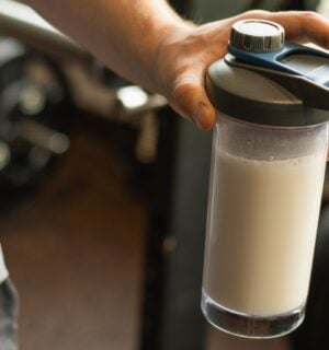 Photo shows a man's hand holding a protein shaker at the gym
