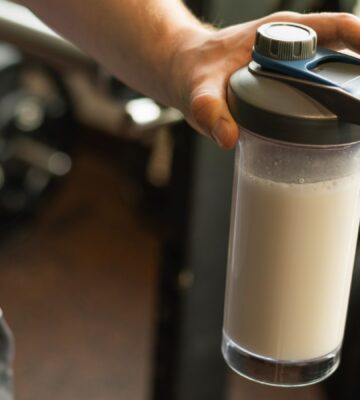Photo shows a man's hand holding a protein shaker at the gym