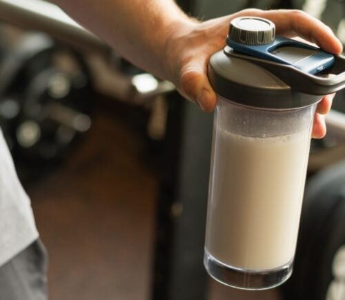 Photo shows a man's hand holding a protein shaker at the gym