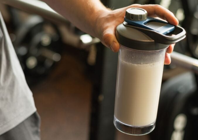 Photo shows a man's hand holding a protein shaker at the gym