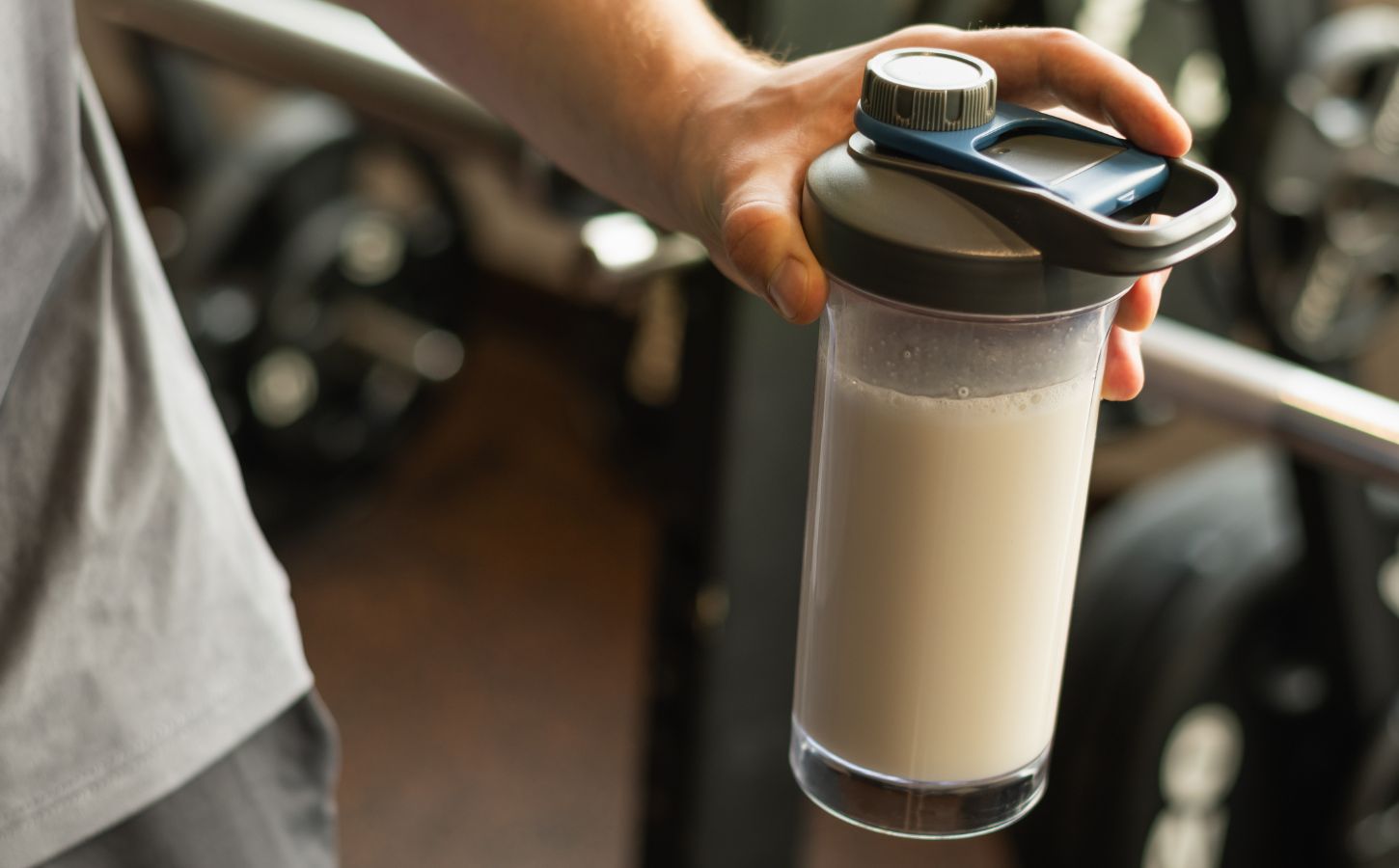Photo shows a man's hand holding a protein shaker at the gym