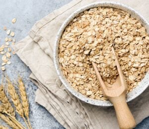 a bowl of uncooked oats with oat plants next to it for an article about why you should eat oatmeal every day