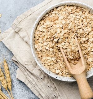 a bowl of uncooked oats with oat plants next to it for an article about why you should eat oatmeal every day