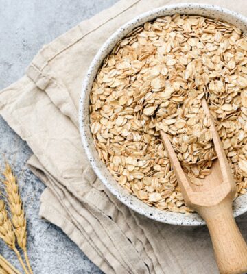 a bowl of uncooked oats with oat plants next to it for an article about why you should eat oatmeal every day