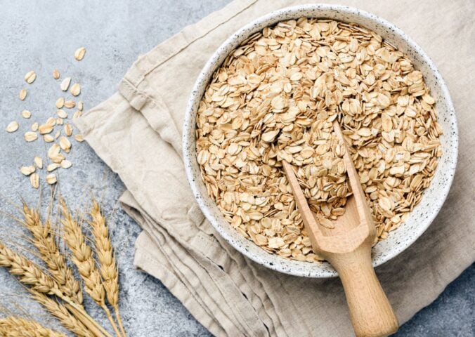 a bowl of uncooked oats with oat plants next to it for an article about why you should eat oatmeal every day
