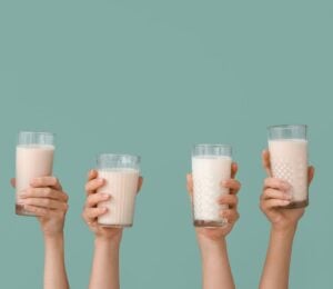 Photo shows a row of hands holding up glasses of milk against a pale blue background