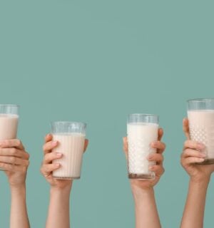 Photo shows a row of hands holding up glasses of milk against a pale blue background