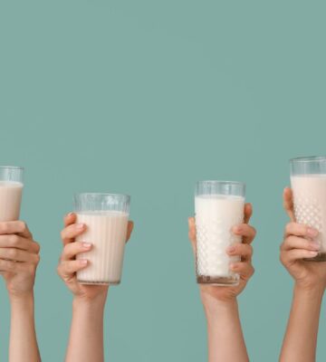 Photo shows a row of hands holding up glasses of milk against a pale blue background