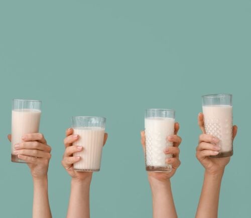 Photo shows a row of hands holding up glasses of milk against a pale blue background