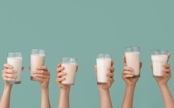 Photo shows a row of hands holding up glasses of milk against a pale blue background