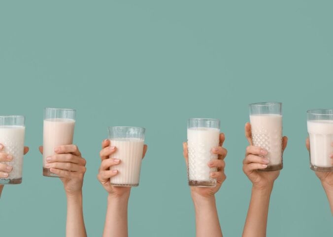 Photo shows a row of hands holding up glasses of milk against a pale blue background