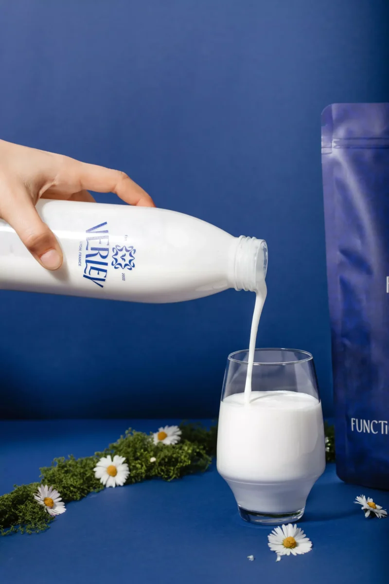 Photo shows someone's hand as they pour a bottle of milk labeled "Verley" into a glass