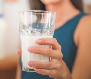 Photo shows a woman holding up a glass of milk to the camera