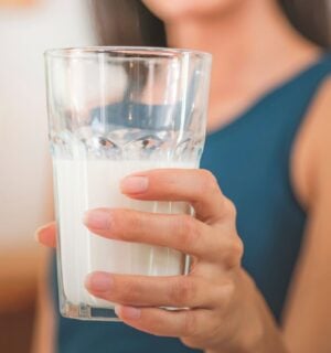 Photo shows a woman holding up a glass of milk to the camera