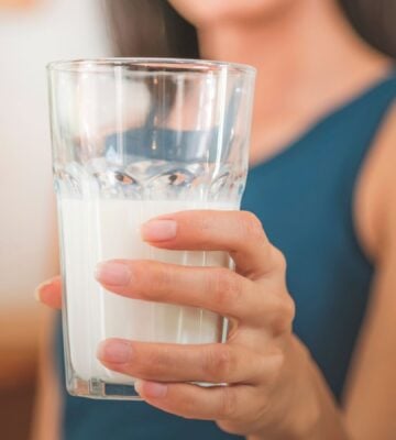 Photo shows a woman holding up a glass of milk to the camera