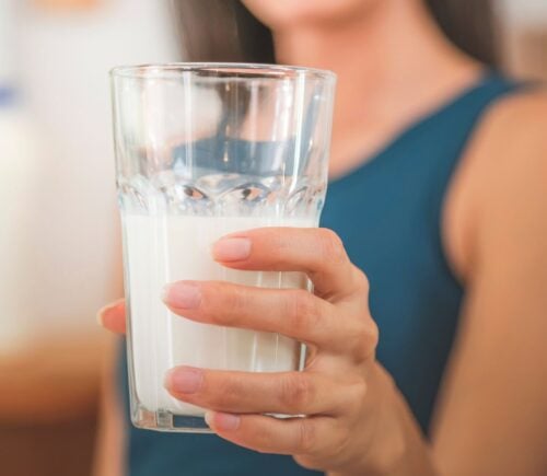 Photo shows a woman holding up a glass of milk to the camera