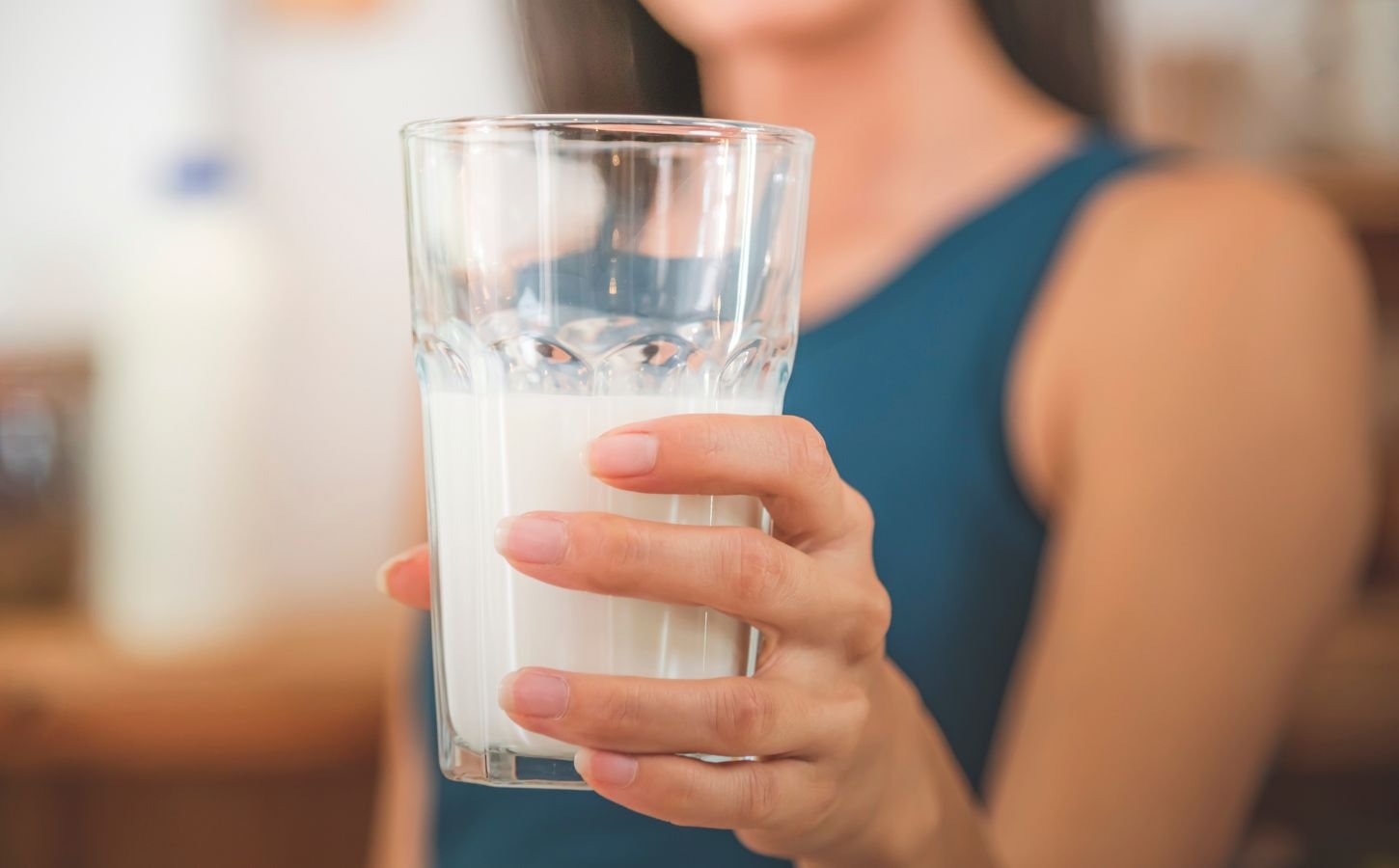 Photo shows a woman holding up a glass of milk to the camera