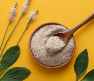 a photo of psyllium husk powder against a yellow background with psyllium plants