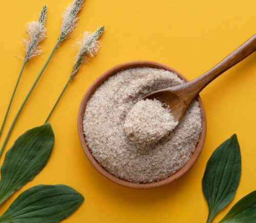 a photo of psyllium husk powder against a yellow background with psyllium plants