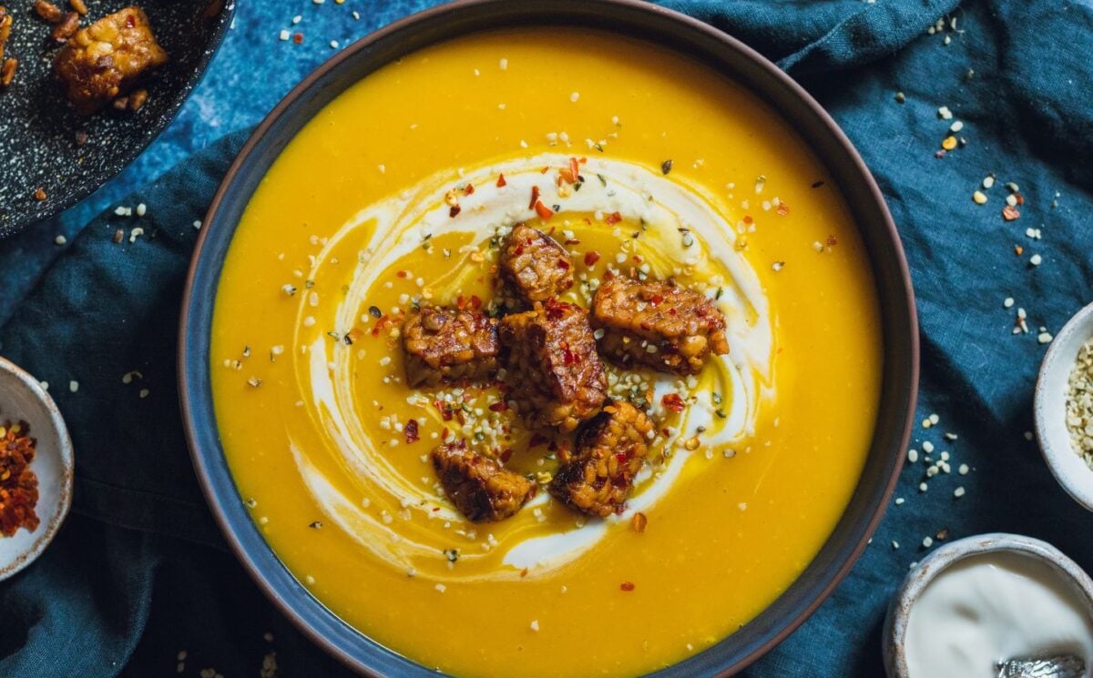 a bowl of spicy swede soup with ginger topped with vegan yogurt, chili, and tempeh chunks for vegan soup recipes